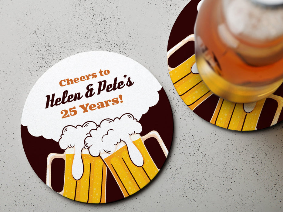 One coaster has a drink on it and an empty coaster sits beside it on a grey background. Coasters say Cheers to Helen & Petes 25 Years!