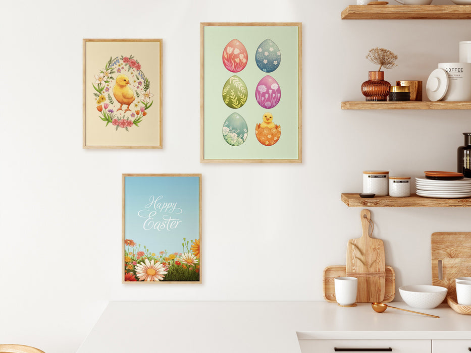 three easter prints with pastel easter artwork in wooden frames on white kitchen wall surrounded by a kitchen counter, and wooden shelves with kitchen items such as plates, bowls, cutting boards, etc