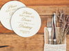 Two coasters are shown stacked on top of each other on a wooden table beside a place setting. Coasters say Please don't take my dance, I'm drinking with wedding couple's names and wedding date on the bottom.