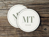 A couple of white coasters sitting on top of a wooden table. Coasters feature a personalized monogram design with a couple's first name initials and date.