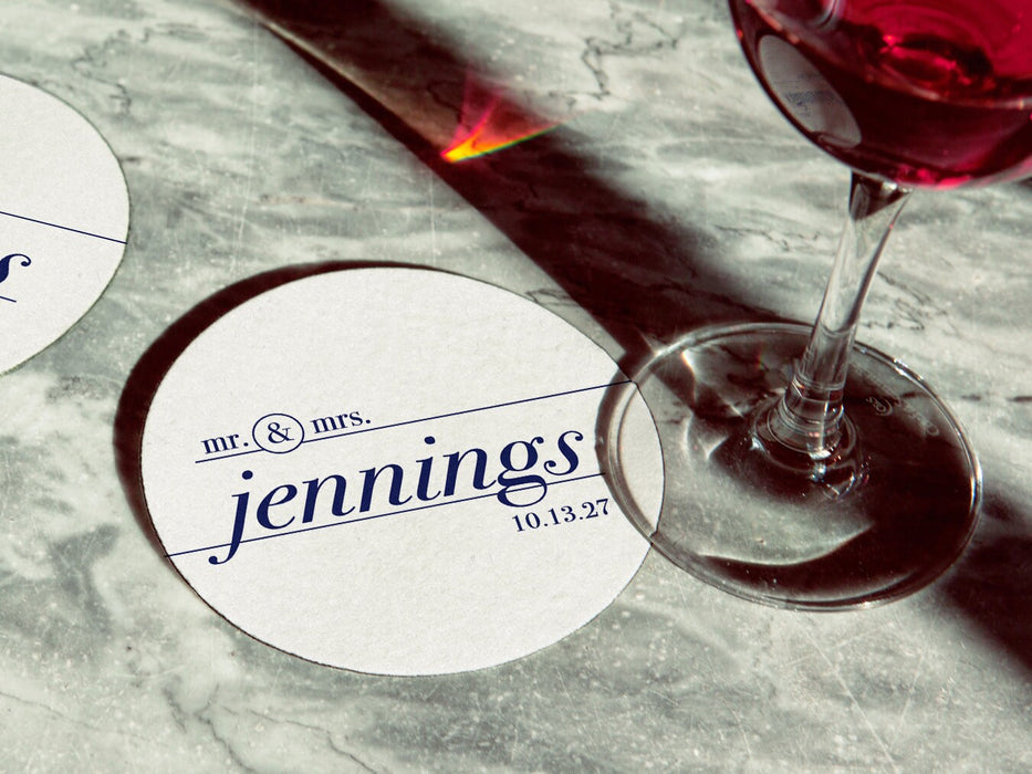 Coaster is shown with a wine glass on top of it and another off to the side. Coasters feature a custom design with a wedding couple's last name and wedding date.