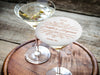One coaster is shown being used as drink cover on top of a martini glass. Coaster features a personalized floral design with the happy couple's first names, wedding date, and location.