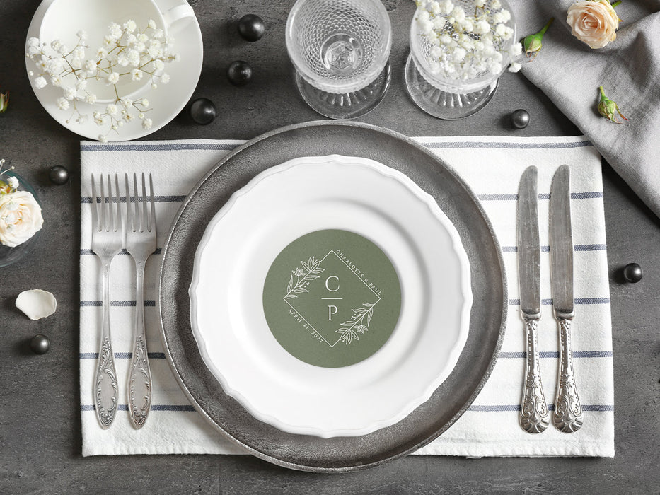 A coaster is shown as a part of a place setting with flowers and silverware. Coaster features a floral diamond design with a monogram, wedding couple's names, and wedding date.