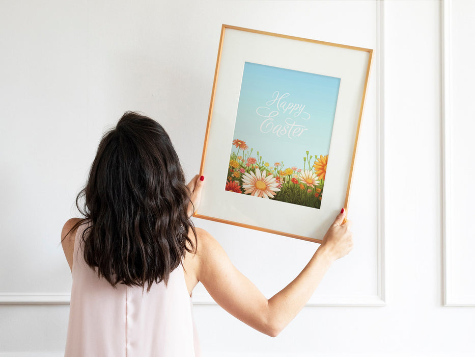woman with black hair and pink shirt holding up a wooden frame with a happy easter print with a colorful meadow of spring flowers