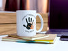 white ceramic mug that says happy first fathers day love Nova with an orange handprint design on top of notebooks on a white desk next to a phone and laptop