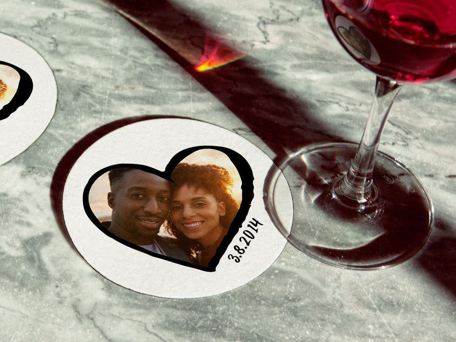 A single coaster with a wine glass on top of it with a coaster off to the side on a marble table. Coasters shown are customizable. Coasters are designed with custom photo, text, and sketched heart frame. Coaster text reads 3.8.2014