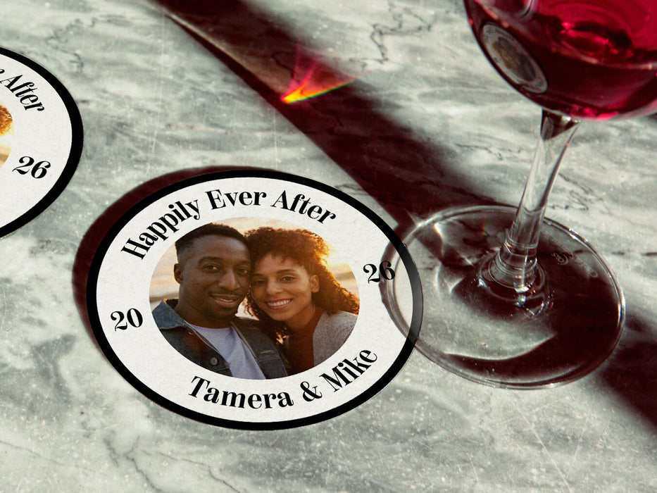 A single coaster with a wine glass on top of it with a coaster off to the side on a marble table. Coasters are designed with custom photo, text, and circular photo frame. Coaster text reads Happily Ever After, 2026, Tamera & Mike.