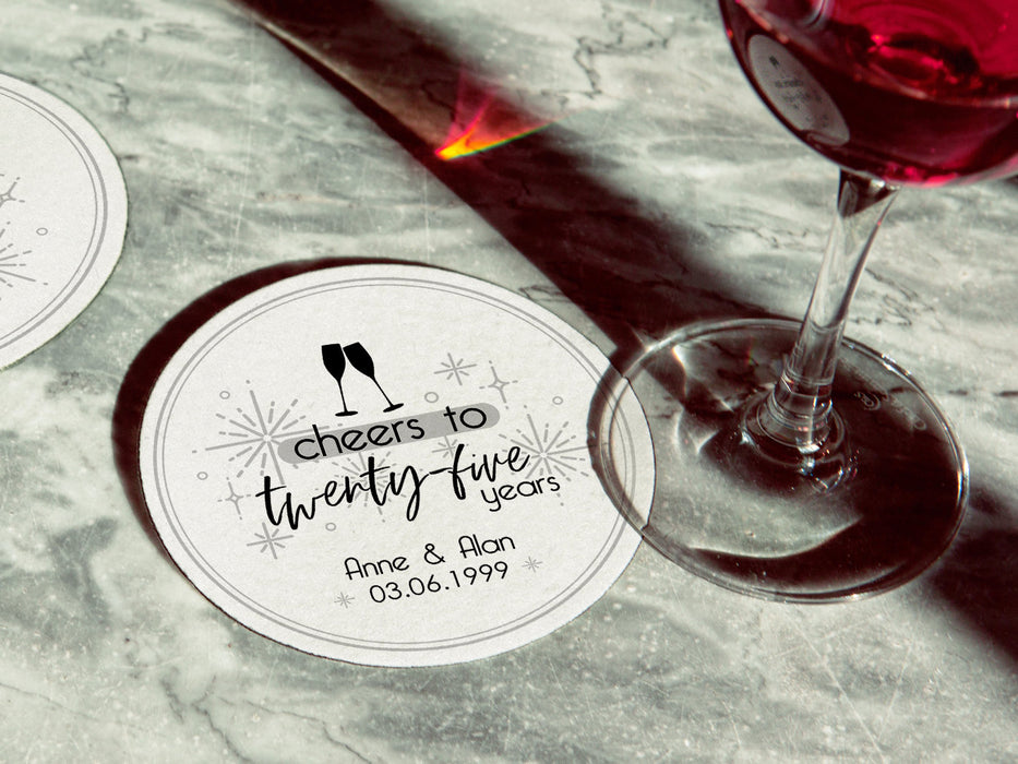 A single coaster with a wine glass on top of it with a coaster off to the side. Coasters shown are customizable. Coasters are designed with gray sparkly elements, wine glasses, and the words Cheers to twenty-five years, custom names, and custom date.