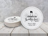 A stack of coasters by a single coaster on a white wooden table. Coasters shown are customizable. Coasters are designed with gray sparkly elements, wine glasses, and the words Cheers to twenty-five years, custom names, and custom date.