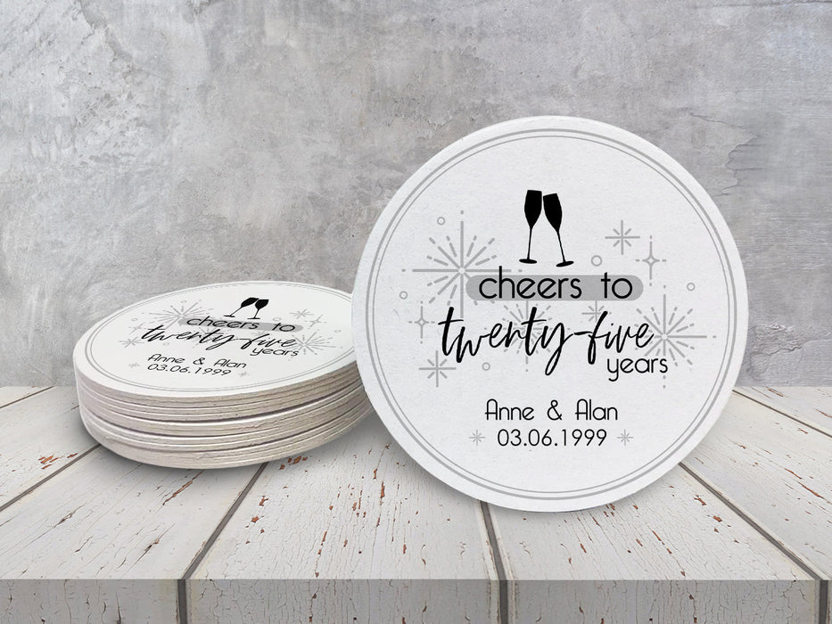 A stack of coasters by a single coaster on a white wooden table. Coasters shown are customizable. Coasters are designed with gray sparkly elements, wine glasses, and the words Cheers to twenty-five years, custom names, and custom date.
