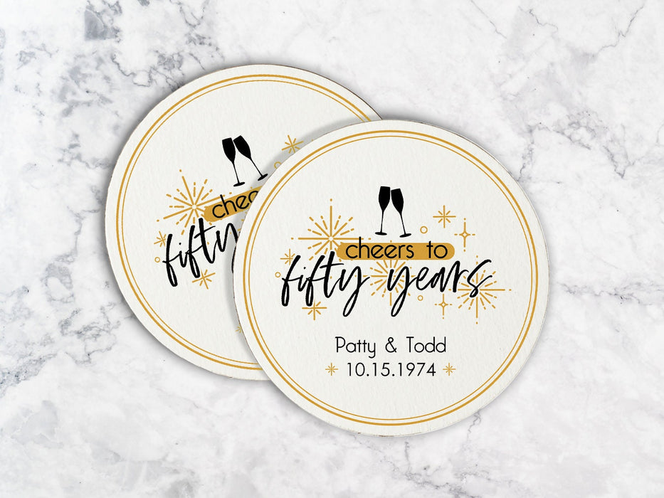 Two coasters sit on a marble surface. Coasters shown are customizable. Coasters are designed with gold sparkly elements, wine glasses, and the words Cheers to fifty years, custom names, and custom date.