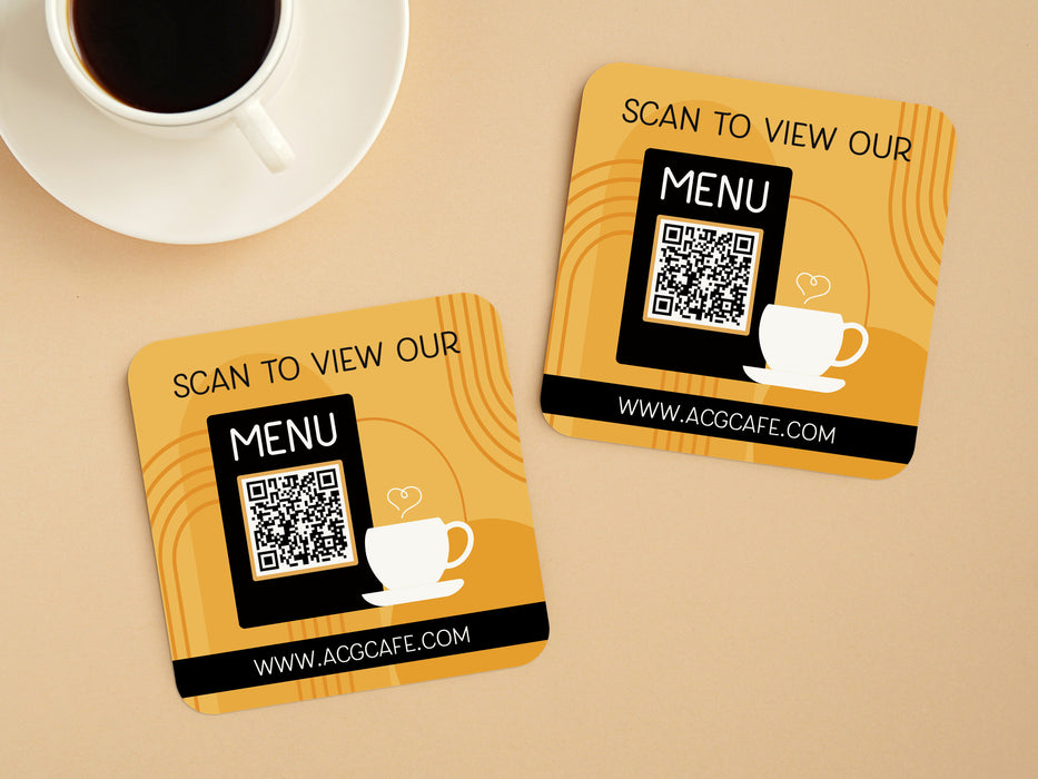 light brown table with a cup of coffee with two custom square QR code coasters that say Scan to view our menu, www.ACGCAFE.com
