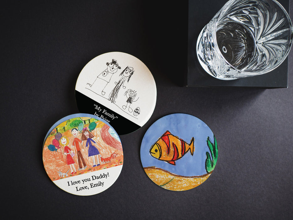 three round paper coasters with kids artwork and custom text printed on the coasters on a black table next to a clear glass of water